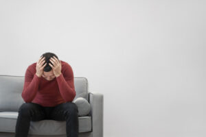 a man sitting on a sofa with his head in his hands, appearing stressed or overwhelmed